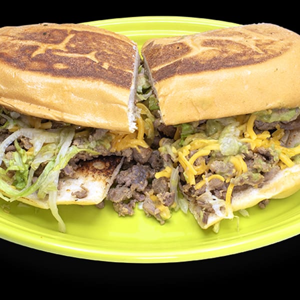 A Mexican torta sandwich, cut in half, filled with meat, cheese, and lettuce on a green plate.