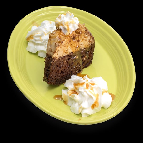 Slice of chocolate flan cake with whipped cream and caramel drizzle on a lime green plate.